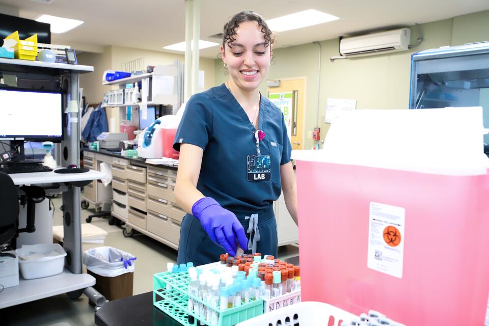 A medical worker in scrubs places a vial into a rack in a medical lab. 